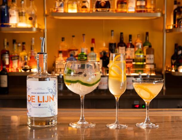 Three cocktails glasses sitting on a bar next to a bottle of De Lijn.