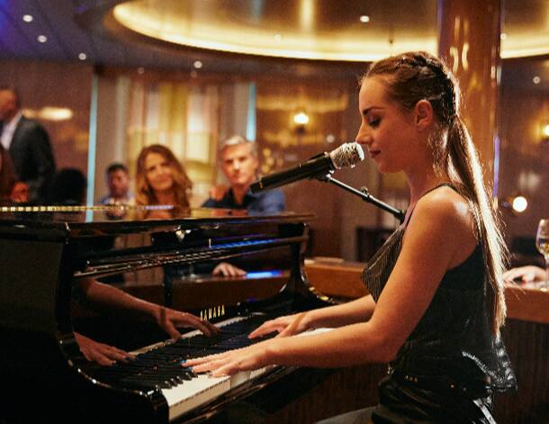 A woman playing the piano and singing while people watch in the background in the Billboard Onboard.