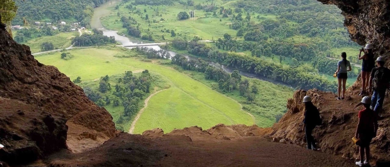Travelers exploring Window Cave in Puerto Rico, overlooking a lush river valley, tropical landscape, and scenic eco-adventure destination.