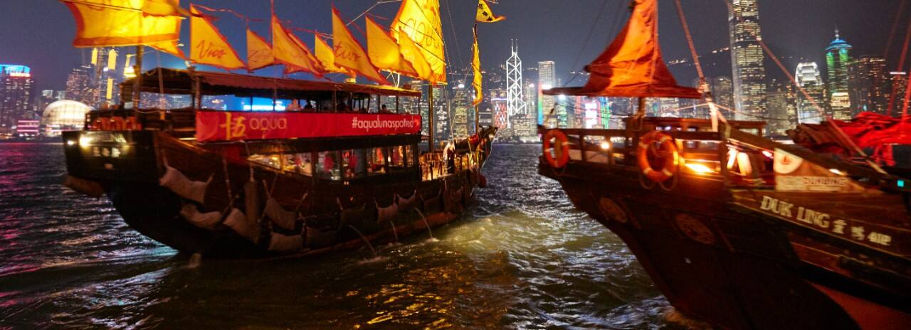 View of two boats in the water at night with the City of Hong Kong in the background.
