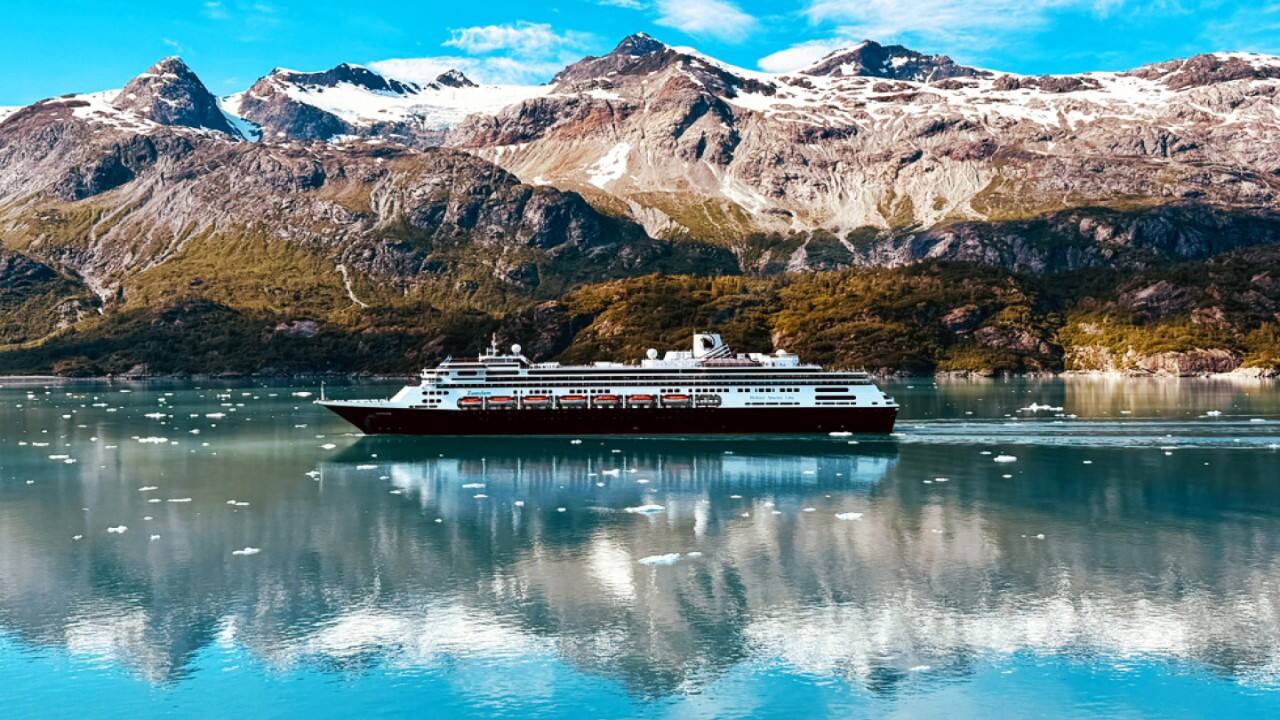 Holland America Line cruise ship sailing through icy Alaskan fjord with snow‑capped mountains.